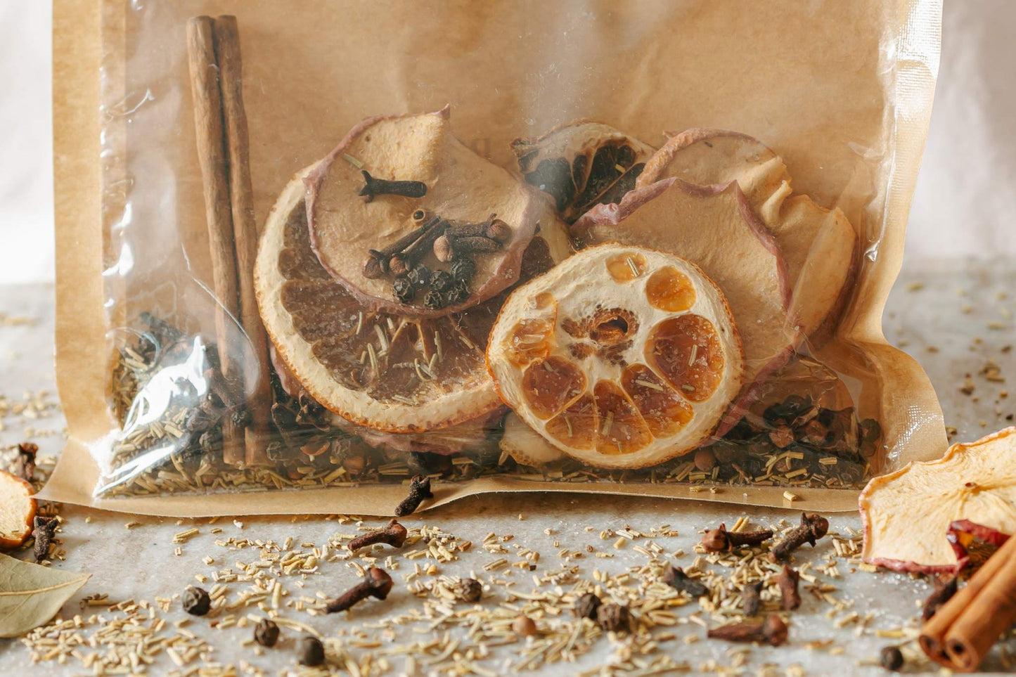 Spice mix with dried oranges, cinnamon sticks, and cloves in a clear bag on a wooden surface.