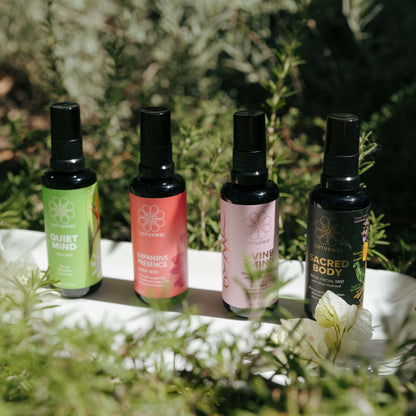 Four spray bottles on a white tray surrounded by greenery