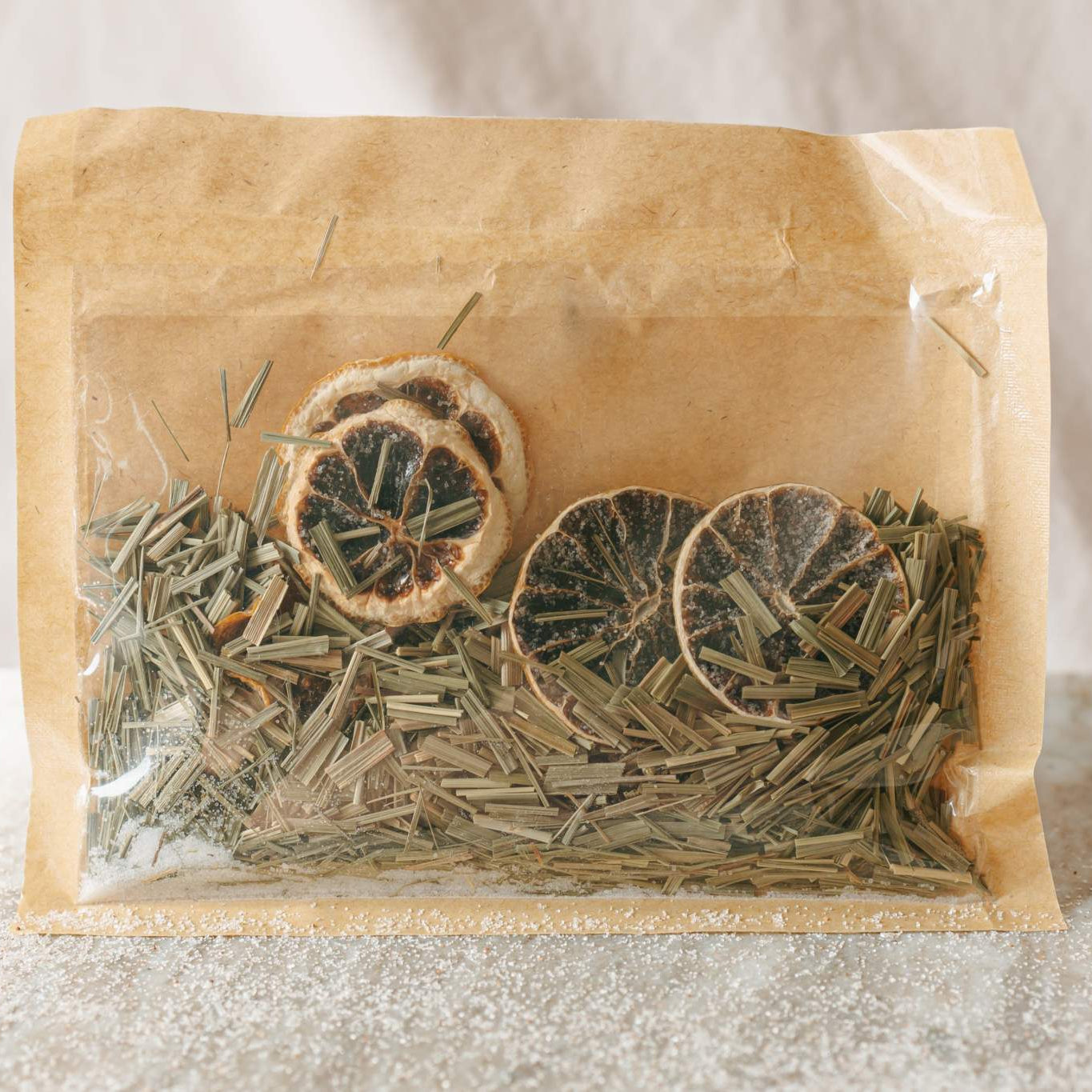 Tea leaves and dried oranges in a clear plastic bag inside a brown paper package on a light background