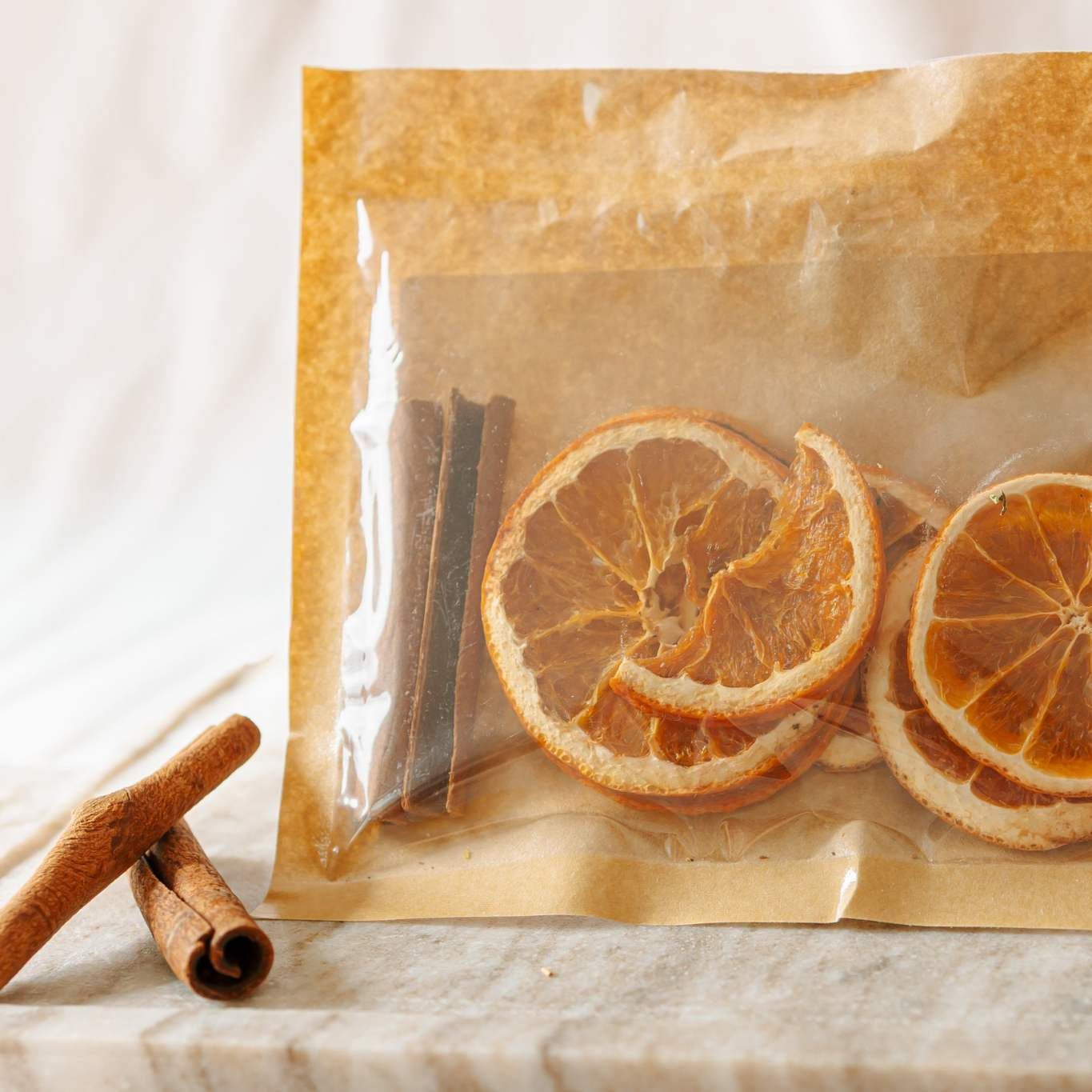 Dried orange slices and cinnamon sticks in a clear plastic bag on a light surface.