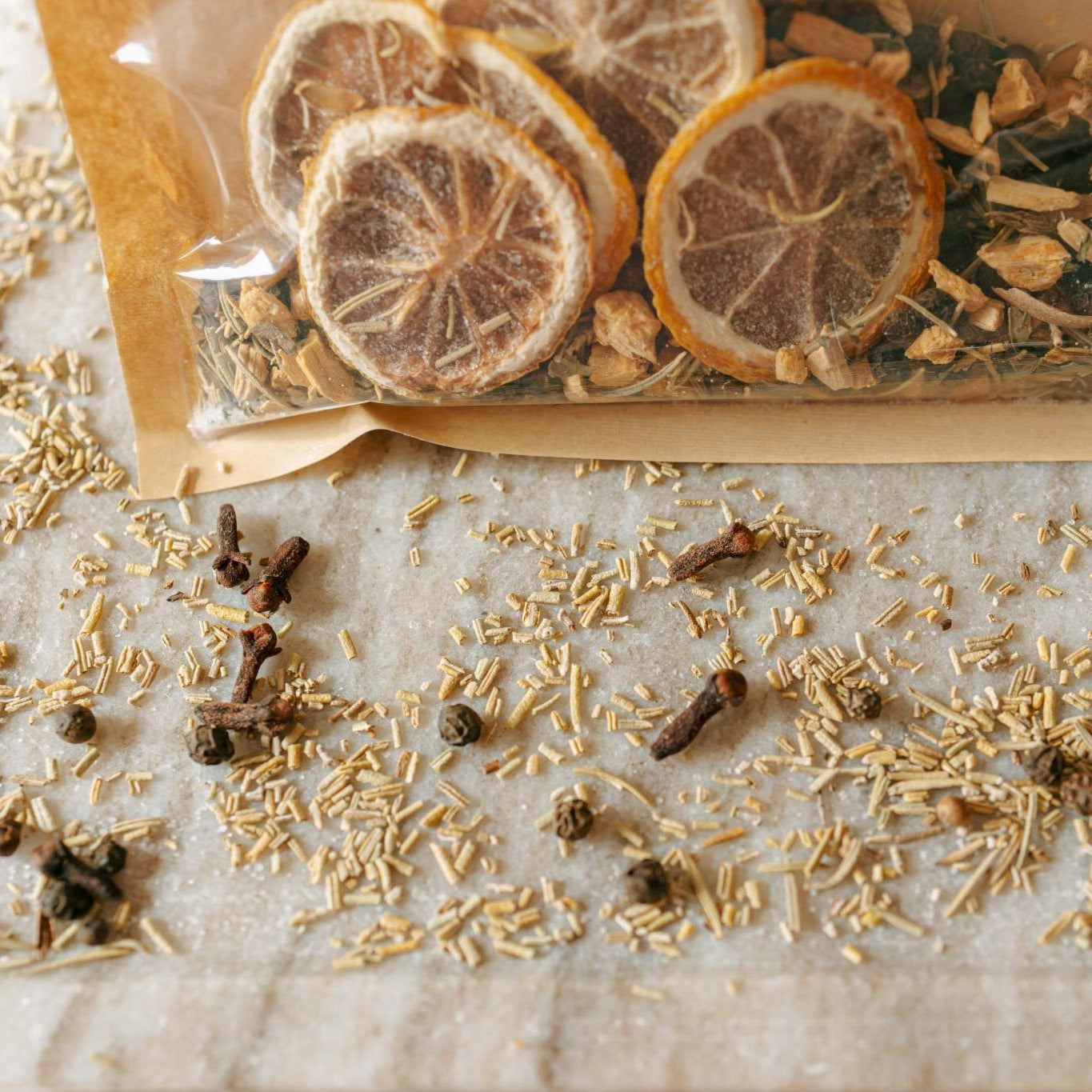 Spices and herbs with a transparent bag containing sliced citrus on a textured surface