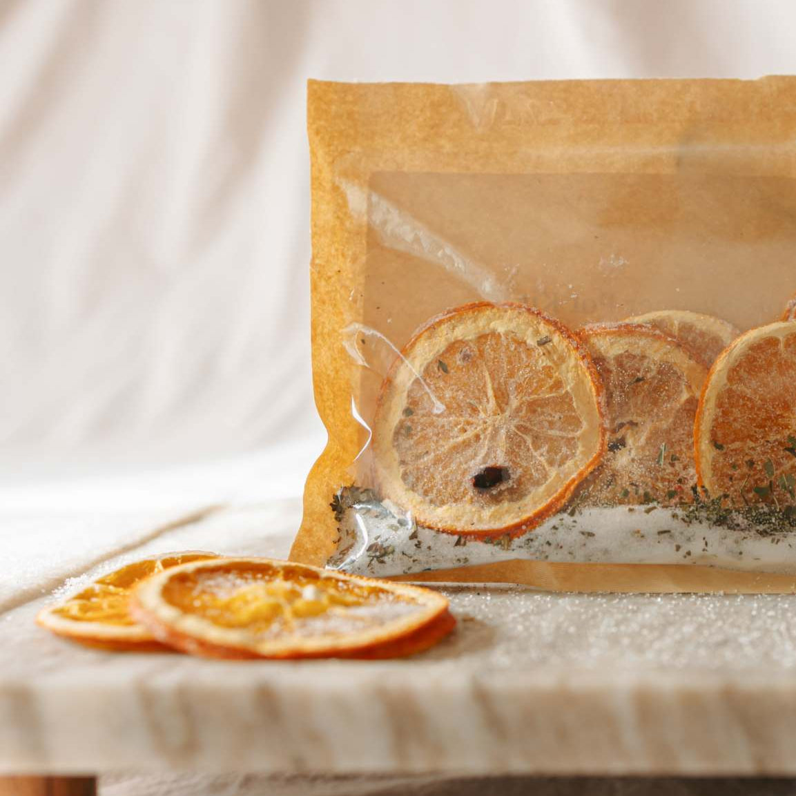 Dried orange slices in a paper bag on a marble surface with a neutral background